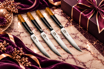 Four Chef Supply Co. Damascus kitchen knives with black and amber wood handles arranged on cream marble with royal amethyst velvet, rose-gold accents, and elegant gift packaging for corporate gift policy planning.