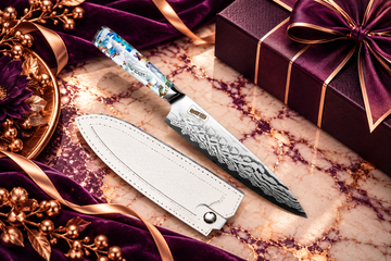 Chef Supply Co. Damascus chef knife with an iridescent blue-and-white handle and white leather sheath, displayed on cream marble with royal purple velvet and rose-gold accents for consistent client appreciation gifting.