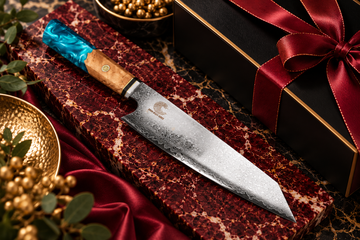 Premium chef’s knife with a turquoise and wood handle on burgundy marble, styled with black and gold gift packaging and a red satin ribbon.
